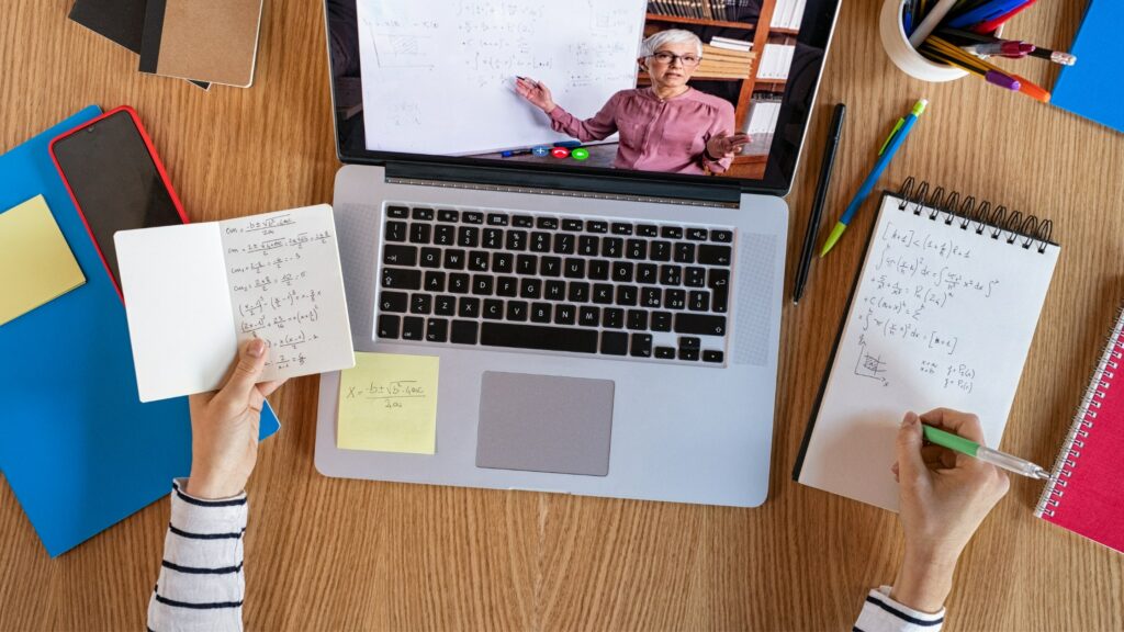 Les mains d’une apprenante prenant des notes sur un cours en ligne avec une formatrice