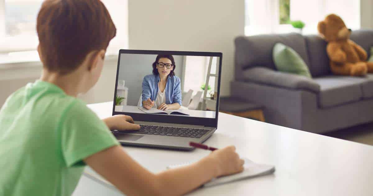 Jeune garçon en train de suivre le cours d'une formatrice en visio sur un ordinateur