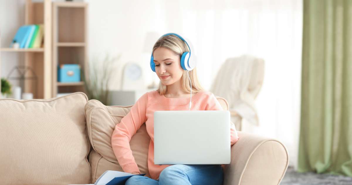 Femme suivant une formation en ligne, sur son canapé avec son casque et son ordinateur sur les genoux