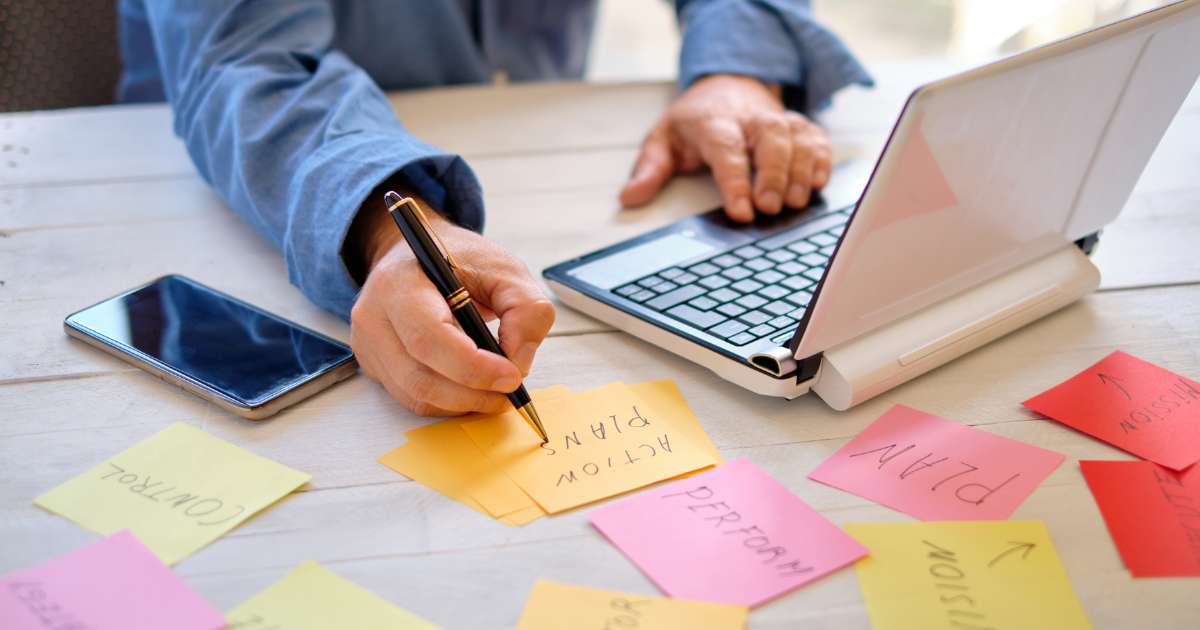 Personne en train de travailler avec des post-it, un stylo, son ordinateur et son téléphone à côté